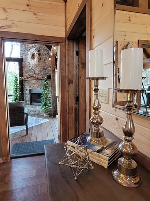 Un intérieur en bois avec une cheminée, une table à manger agrémentée d’objets décoratifs, et une vue sur un mur en pierre et un espace extérieur.