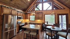 A spacious kitchen with wooden cabinets, stainless steel appliances, and a large island with bar stools. - Incredible firepit, luxurious cabin, indoor&outdoor fireplaces. Minutes to town. (Morganton)