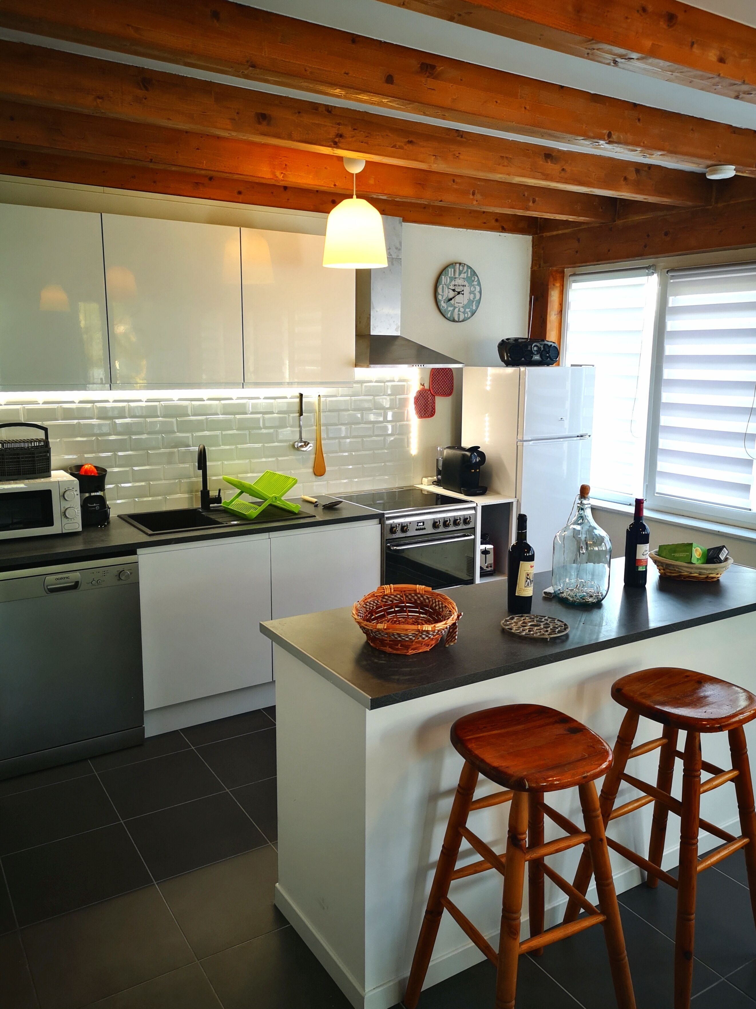 A modern kitchen with white cabinetry, a central island with stools, a microwave, a stove, and a sink.