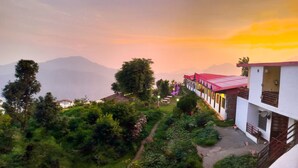 A hillside hotel with a red-roofed building, lush greenery, and a view of distant mountains. - Haut Monde King's Paradise Resort  (Tehri)