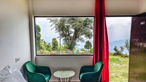 A hotel room with a large window, a bed, two green chairs, and a small table. - Haut Monde King's Paradise Resort  (Tehri)