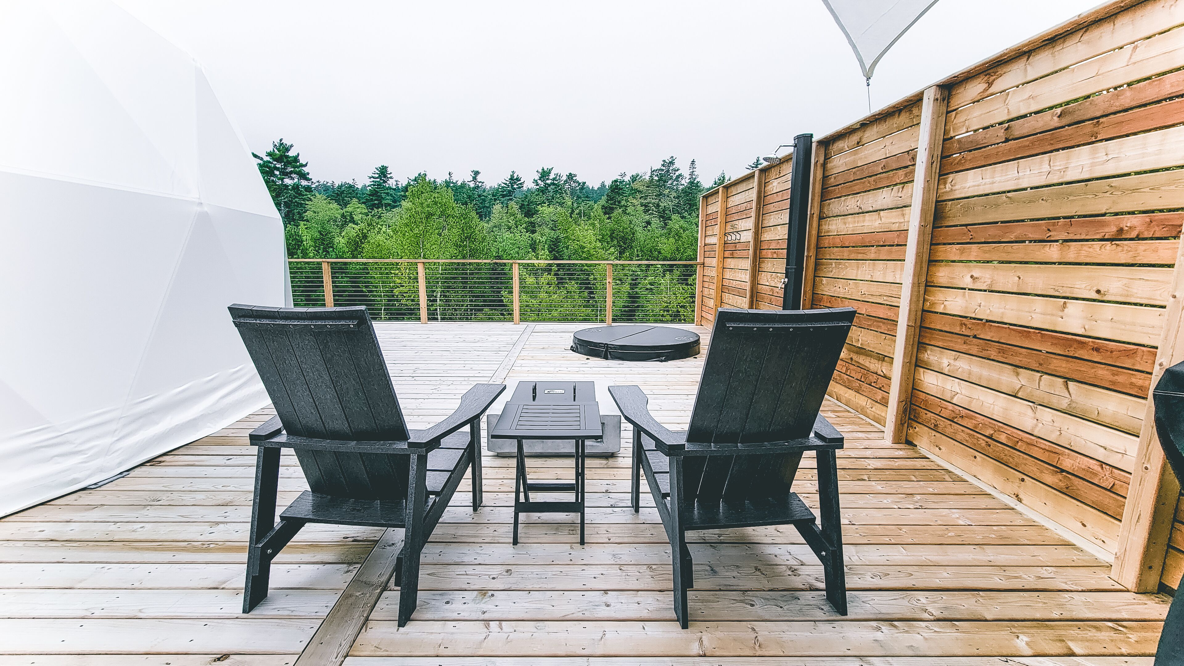 A wooden deck with two black chairs and a small table, surrounded by a wooden fence and a white tent.