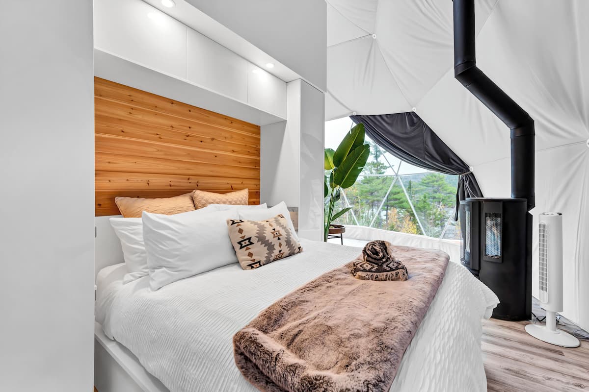 Ein modernes Schlafzimmer mit einem Holzkopfteil, weißer Bettwäsche, einer kuscheligen Decke und einem schwarzen Heizgerät.