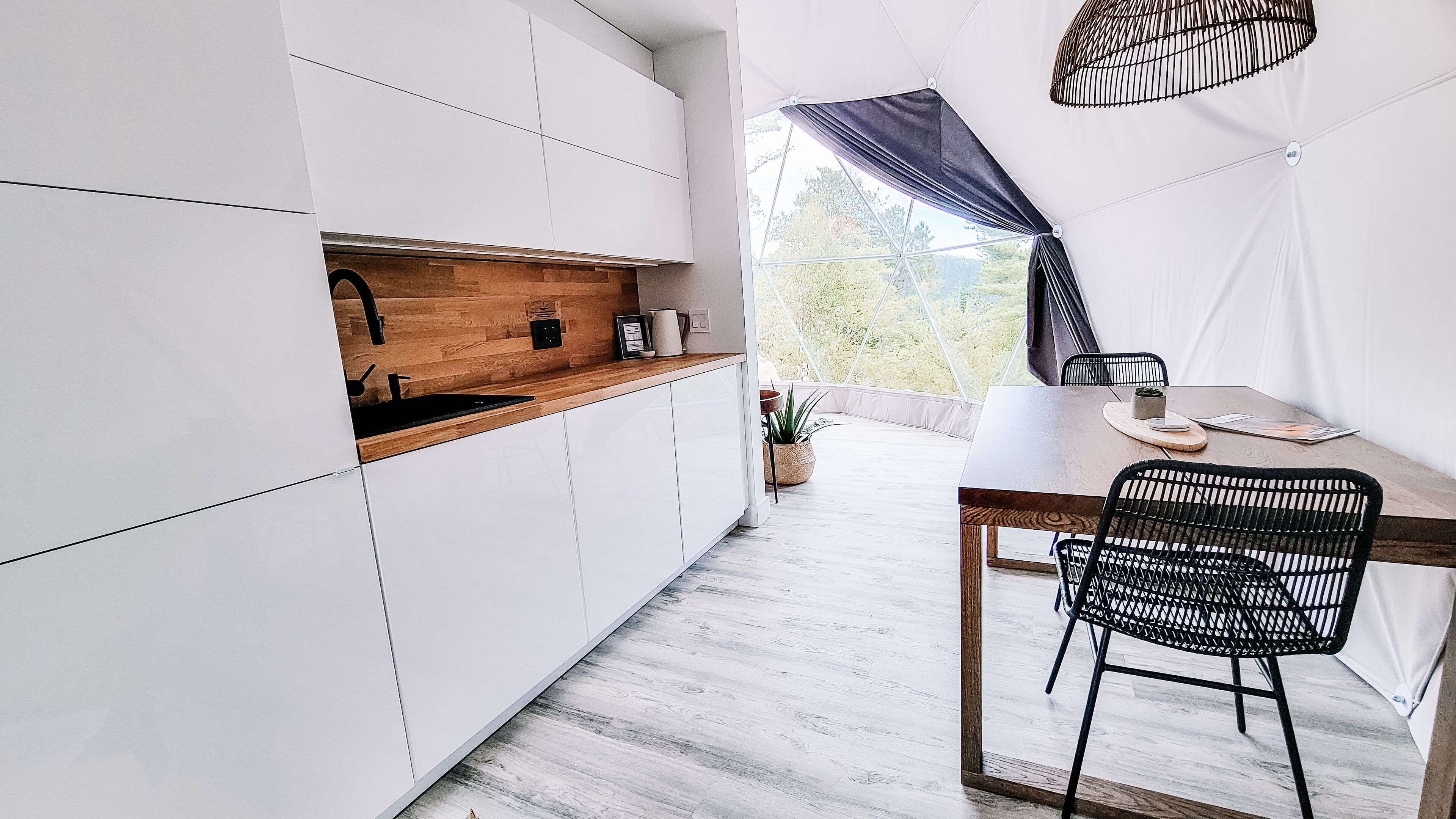 A modern kitchen with white cabinets, a wooden countertop, and a view of greenery outside.