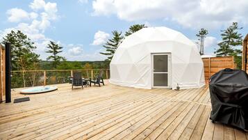 A geodesic dome structure on a wooden deck with a hot tub, outdoor seating, and a grill.