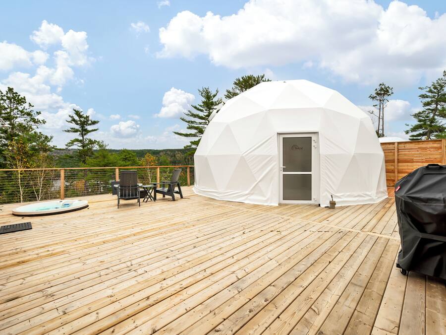 A geodesic dome structure on a wooden deck with a hot tub, outdoor seating, and a grill.