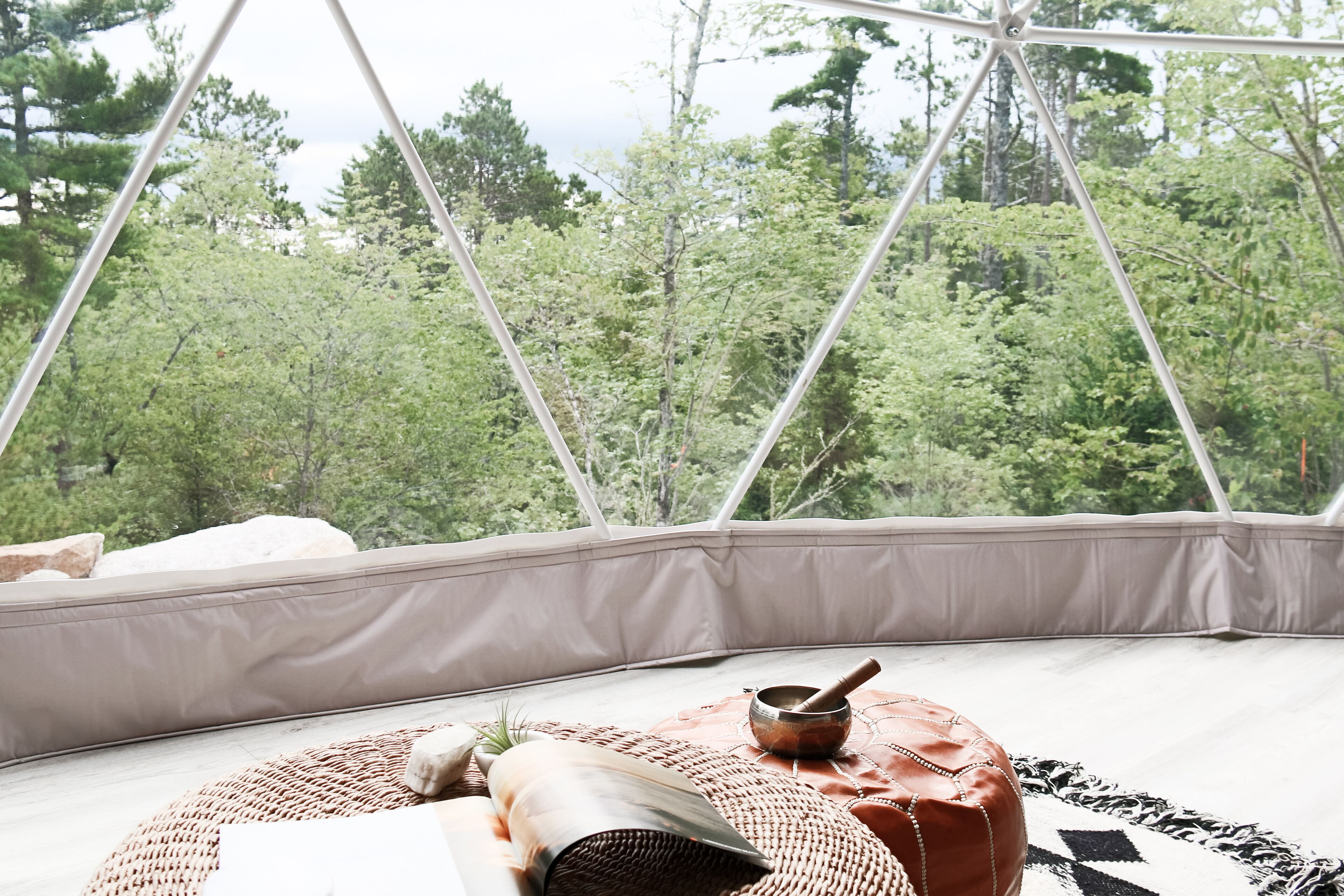 A cozy room with a view of a forest, a woven rug, a pillow, and a small table with a bowl.