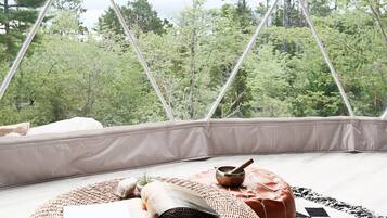 A cozy room with a view of a forest, a woven rug, a pillow, and a small table with a bowl.