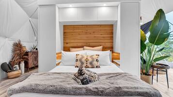 A modern bedroom with a wooden headboard, white bedding, and a large plant by the window.