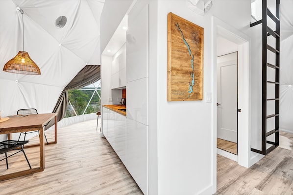 A modern kitchen with white cabinetry, a wooden table, and a hanging pendant light.