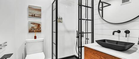 A modern bathroom with a glass-enclosed shower, a white toilet, a wooden vanity, and a black sink.