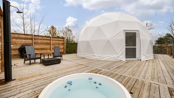 Relax in a hot tub surrounded by a serene natural setting, with a geodesic dome structure nearby.