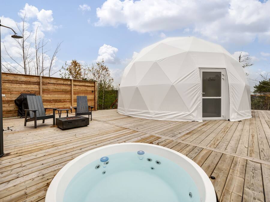 Een koepelvormige tent met een deur, een hottub en tuinmeubilair op een houten terras.