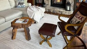 Ein gemütliches Wohnzimmer mit Kamin aus Stein, einer Couch, einem Couchtisch und einem Ledersessel.