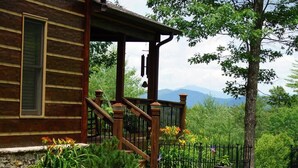 Eine Holzhütte mit Veranda, umgeben von einem Garten mit verschiedenen Pflanzen und Blumen.