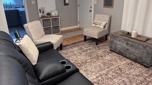 Een woonkamer met een zwarte leren bank, gestreepten fauteuils, een houten salontafel en een decoratief vloerkleed.