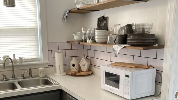 Una cocina moderna con armarios grises, encimera blanca, microondas integrado y una ventana con persianas.