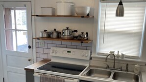 Una cocina con estufa, horno y lavaplatos. Hay repisas sobre la estufa con ollas y sartenes.