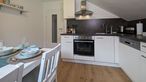 Een kleine keuken met witte kastjes, een zwarte oven en een rvs-afzuigkap.