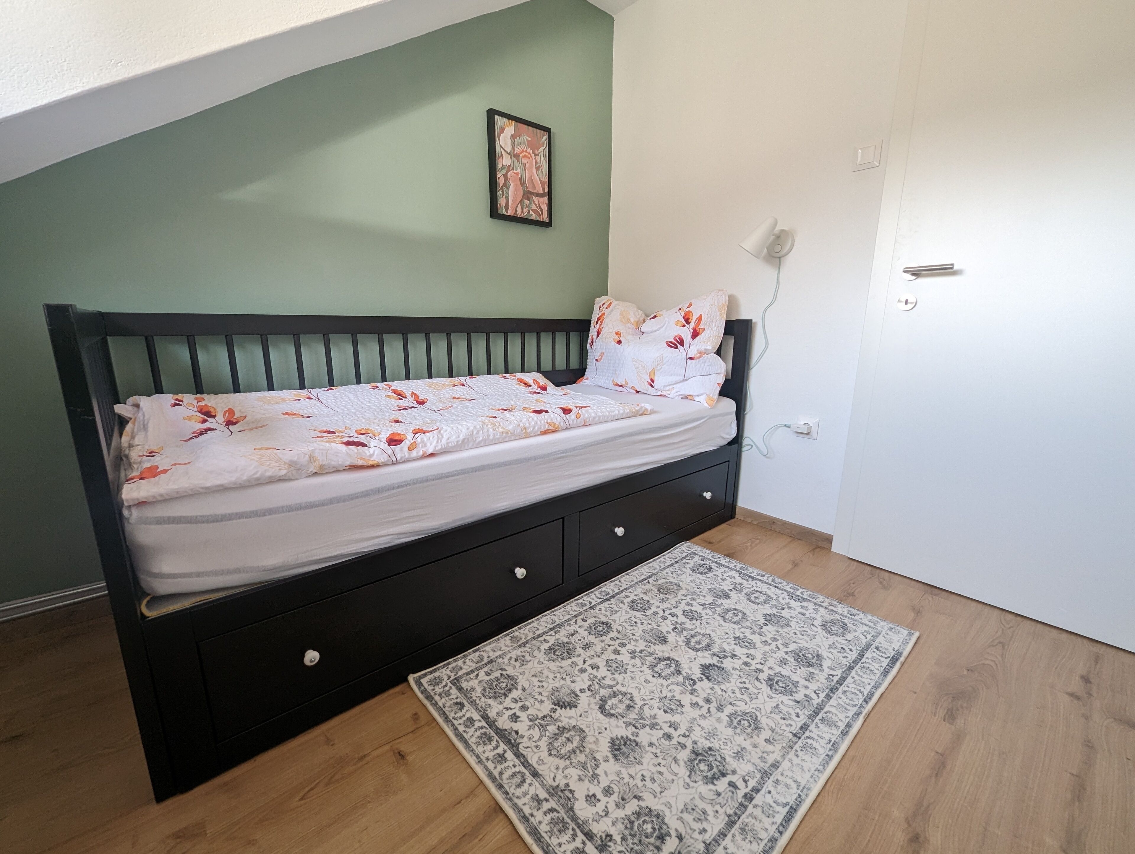 A bedroom with a bed, a small rug, a wall art piece, and a door.