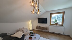 Een moderne woonkamer met een bank, een salontafel, een televisie en een raam met uitzicht op een bos.