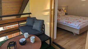 Een gezellige slaapkamer met een houten plafond, een bed met bloemenbeddengoed en een klein zithoekje met kussens en een tafeltje met mokken.