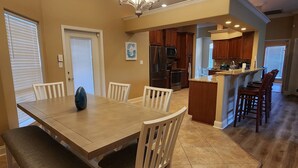 Zona pranzo con tavolo e sedie in legno, una panca, un lampadario e una cucina sullo sfondo.