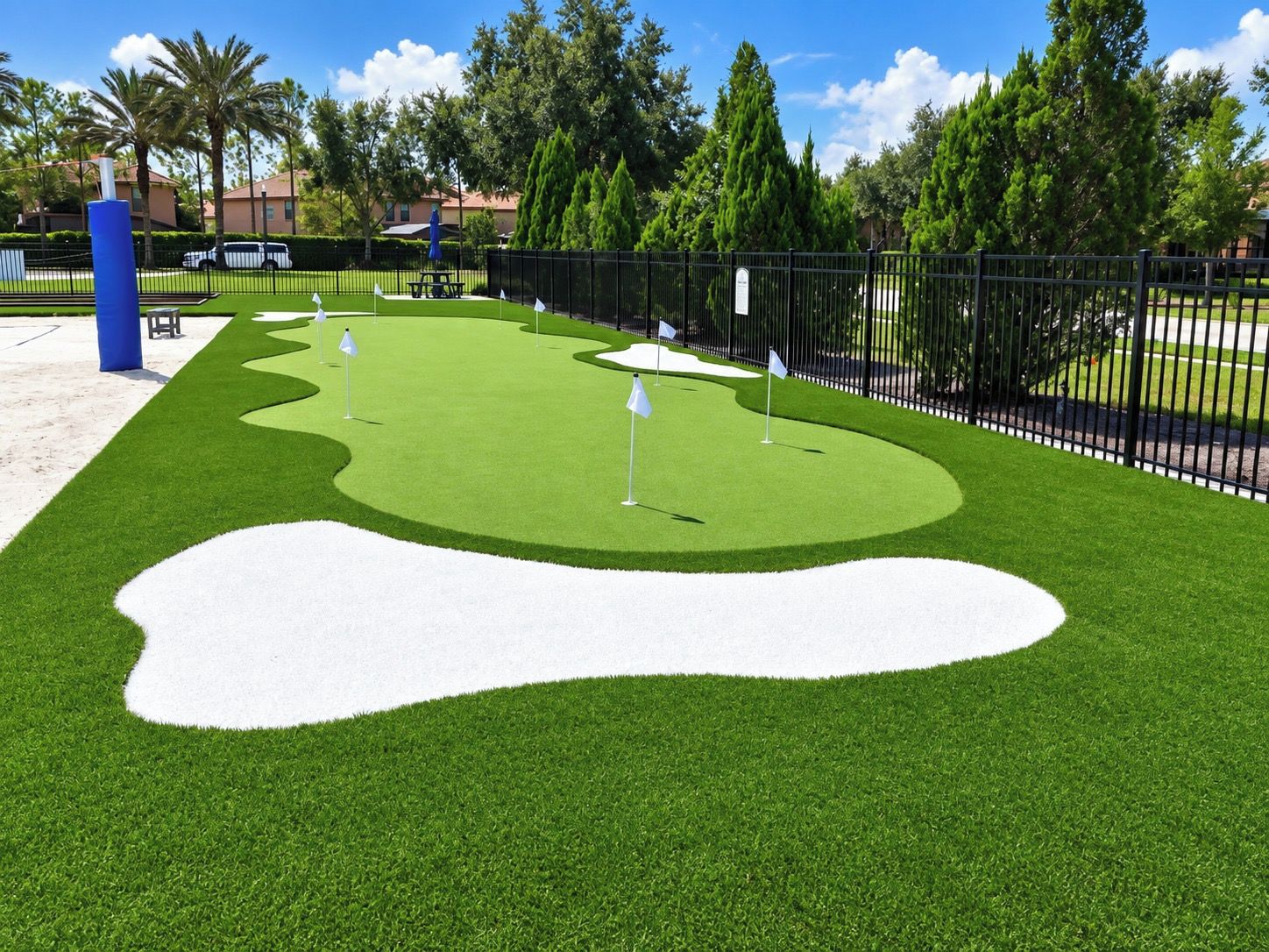 Un parcours de golf avec un bunker de sable, des drapeaux et une clôture.