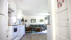Una cocina con armarios blancos, una mesa de comedor de madera y un sofá gris en la sala.