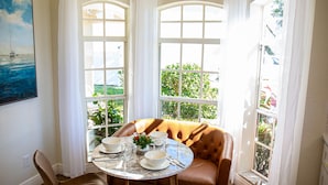 Un comedor con una mesa redonda dispuesta para cuatro personas, rodeada de sillas de cuero. Hay dos ventanas grandes con marcos blancos que dejan entrar luz natural.