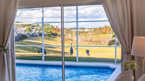 Un dormitorio con un ventanal grande que da a una piscina y un campo de golf.