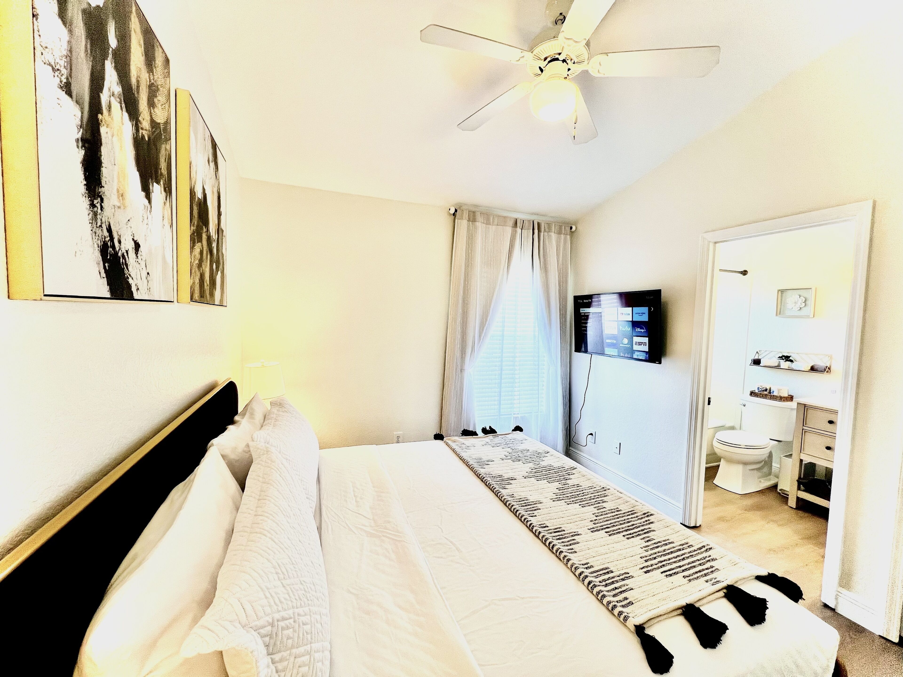 A hotel room with a bed, a ceiling fan, a TV, and a bathroom visible through an open door.