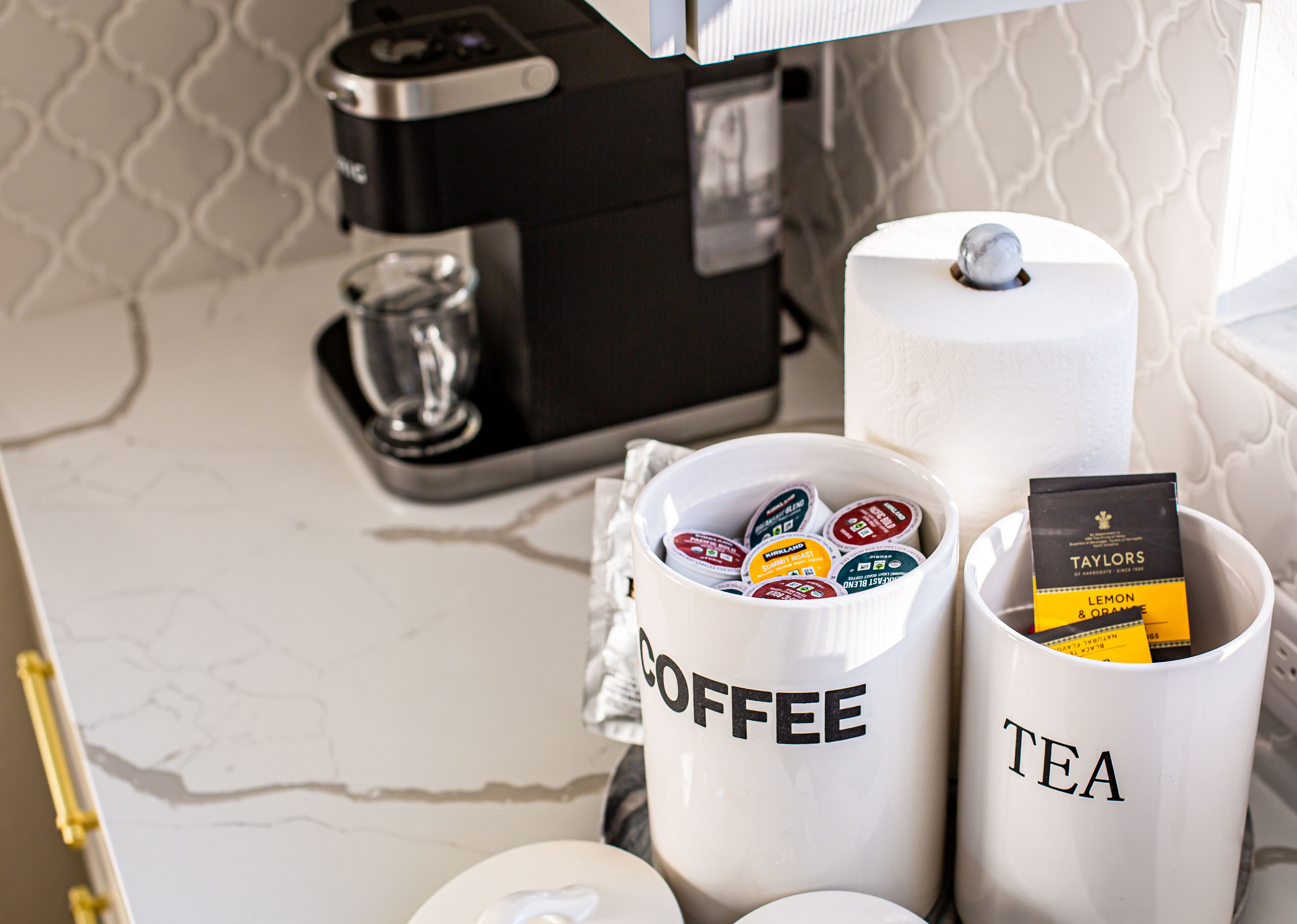 Una estación de café y té con recipientes etiquetados, una cafetera y una taza.