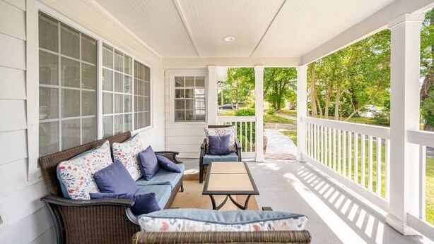 A covered porch with wicker furniture, a small table, and a view of a green landscape.