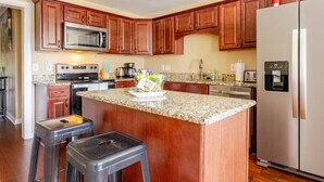 A kitchen with wooden cabinets, a granite countertop, a stainless steel refrigerator, a microwave, a stove, and a water dispenser.
