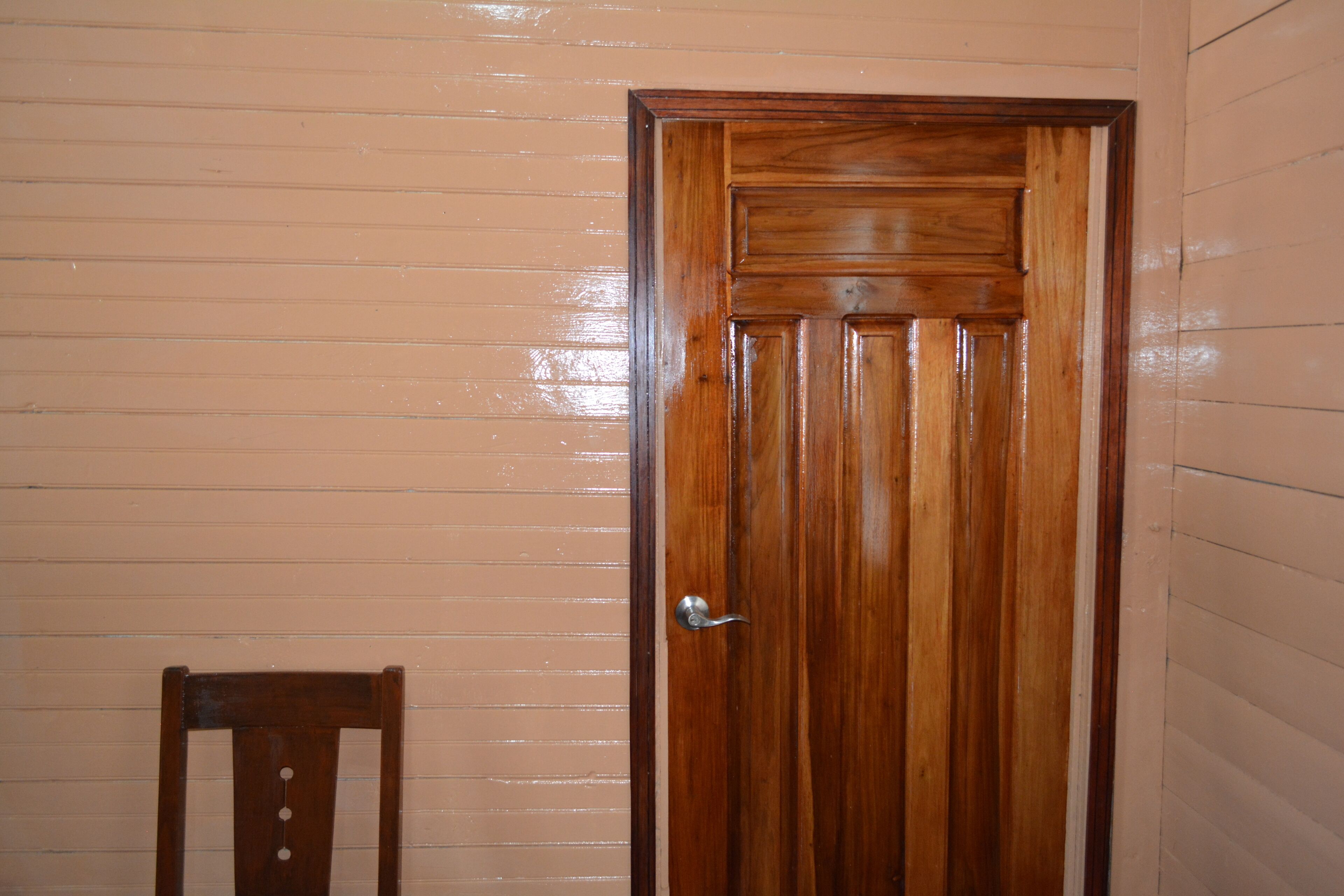 A wooden door with a silver handle, a wooden chair, and a beige wall.