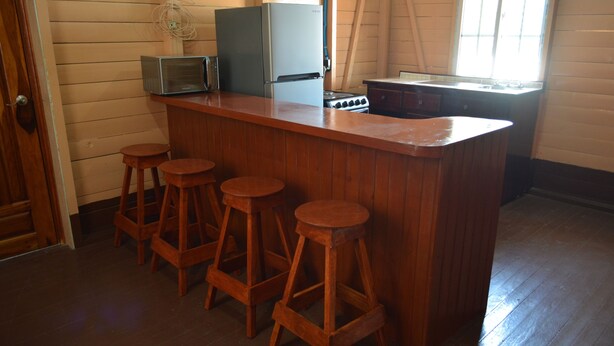 A kitchen with wooden bar stools, a refrigerator, a microwave, and a stove.