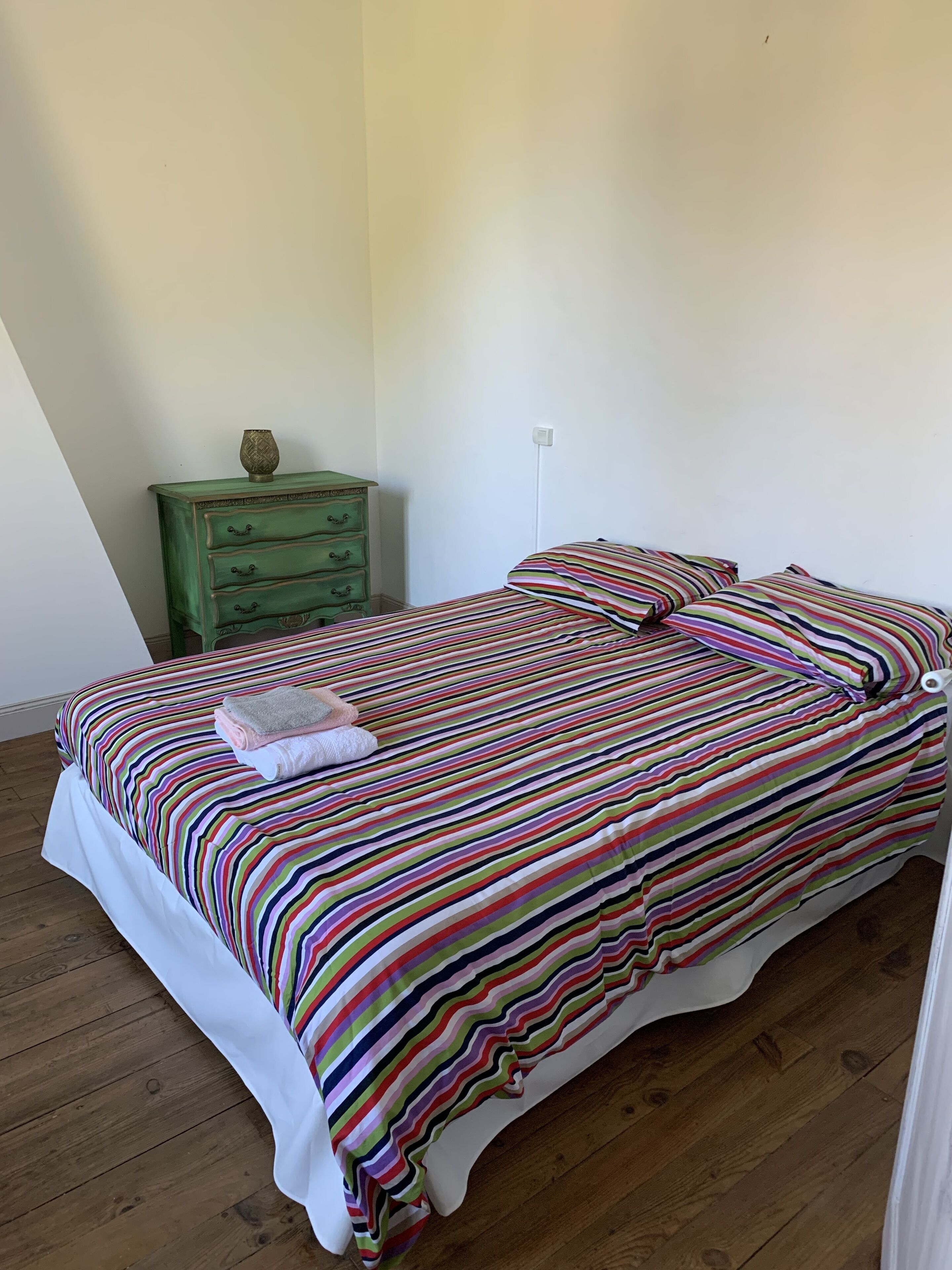 Ein Schlafzimmer mit einem gestreiften Bettüberzug, einer grünen Kommode und einer weißen Wand.