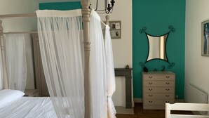 Ein Schlafzimmer mit Himmelbett, Nachttisch, Schminktisch und Spiegel an der Wand.