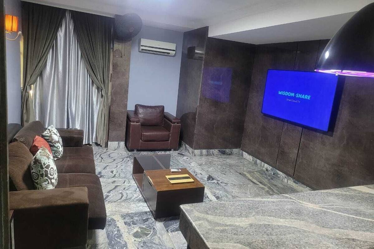 A modern living room with a sofa, armchair, and a coffee table. A flat-screen TV is mounted on the wall.