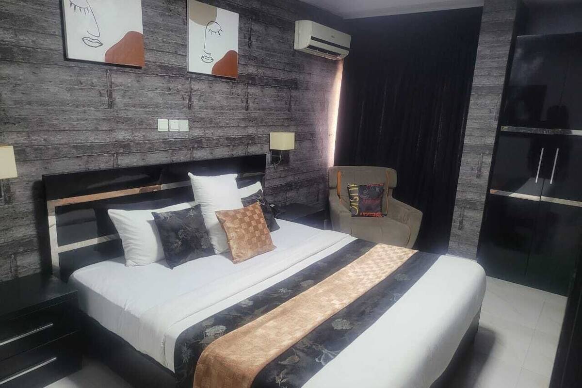 A modern bedroom with a large bed, dark wooden headboard, and a dark curtain on the window.