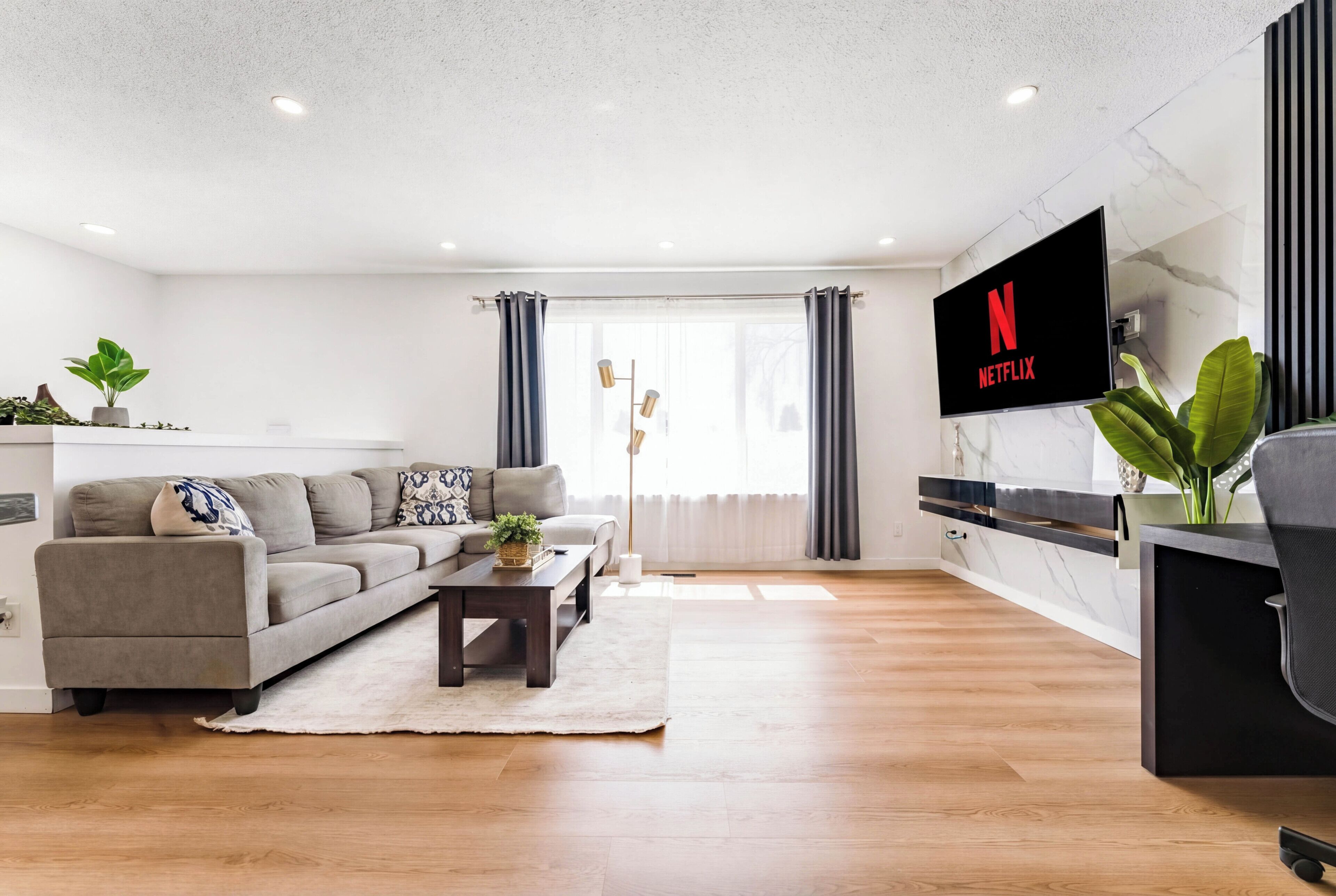 Een moderne woonkamer met een bank, salontafel en een aan de muur bevestigde televisie.