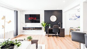 Una sala de estar moderna con un televisor de pantalla plana, un espejo redondo, una zona de comedor y piso de madera.
