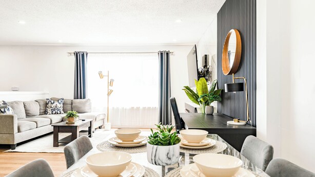 Una sala de estar moderna con comedor, sofás grises, una mesa de centro y un ventanal con cortinas.