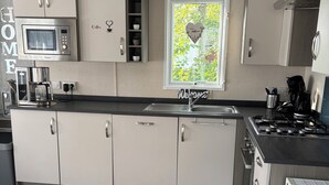 Moderni keittiö, jossa on valkoiset kaapit, sisäänrakennettu mikroaaltouuni, kahvinkeitin ja kaasuliesi.