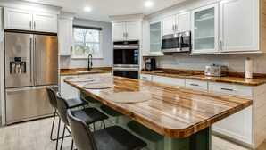 Una cucina moderna con mobili bianchi, elettrodomestici in acciaio inossidabile, un piano di lavoro in legno e sgabelli da bar.