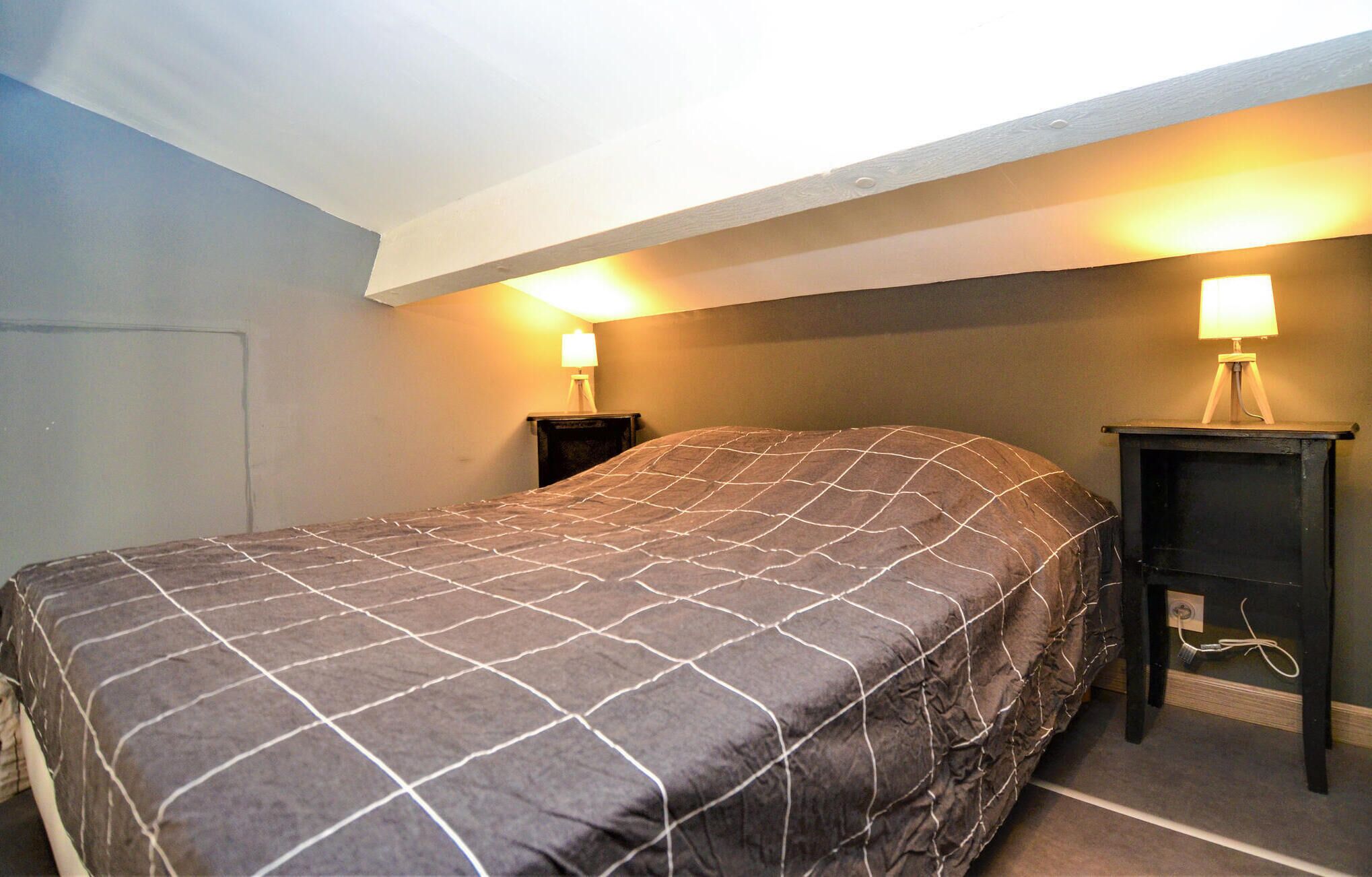 A bedroom with a bed, two bedside lamps, and a small wooden nightstand.