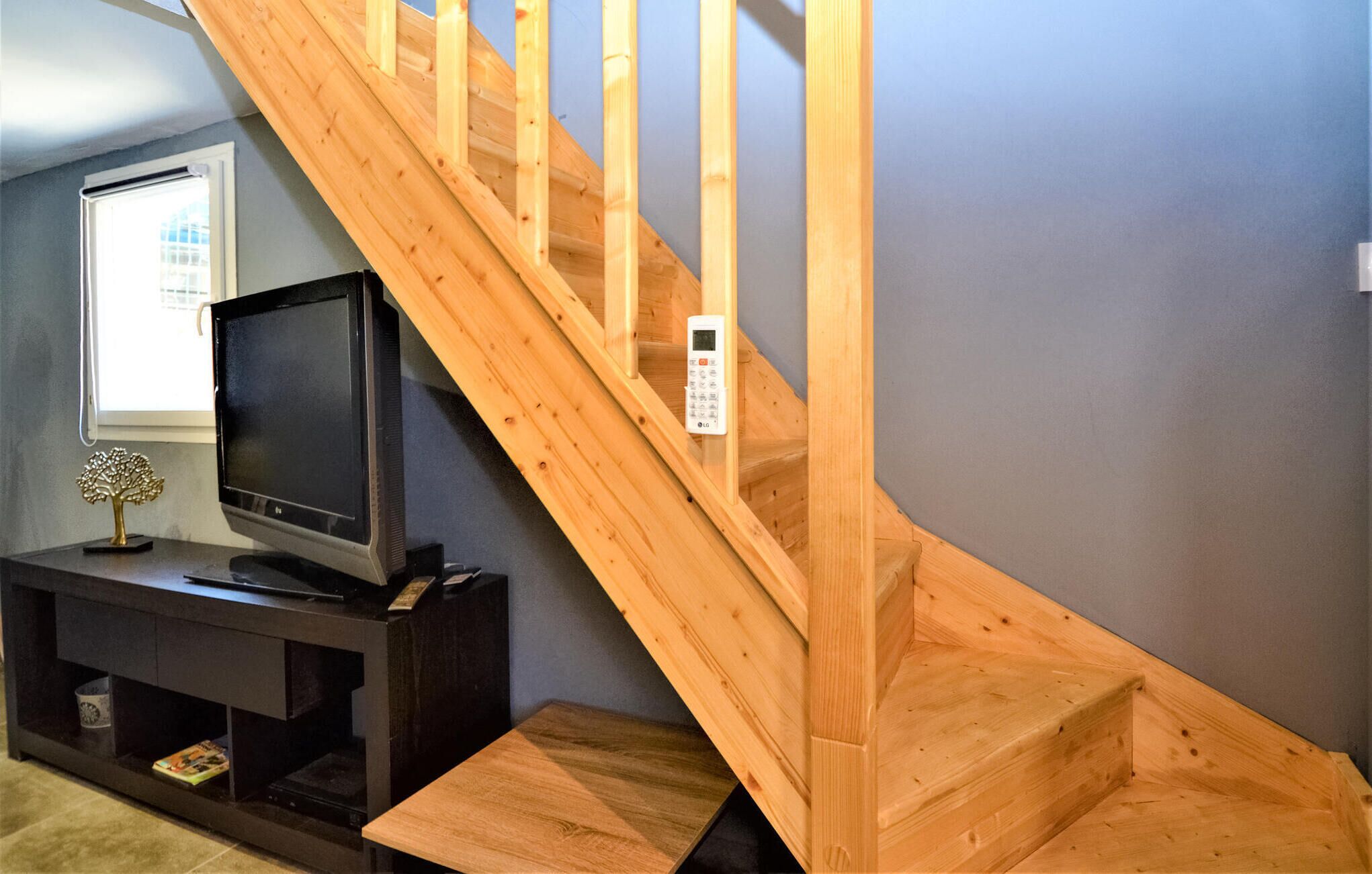 A wooden staircase with a handrail, a television on a stand, and a small decorative tree.