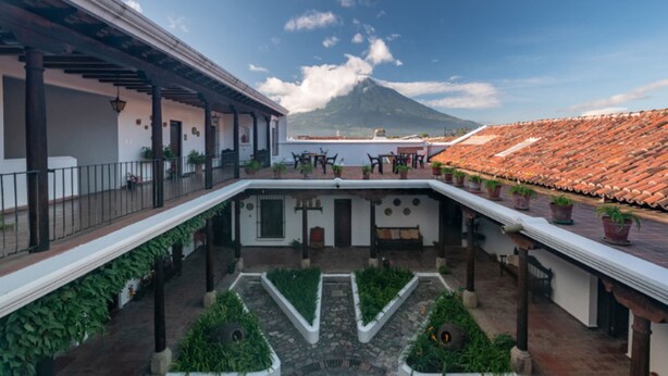 A courtyard with a view of a mountain, potted plants, and a tiled roof. - Casita Escondida (Antigua Guatemala)