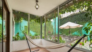 A hammock in a room with large windows, wooden flooring, and a view of greenery outside. - Casita Escondida (Antigua Guatemala)